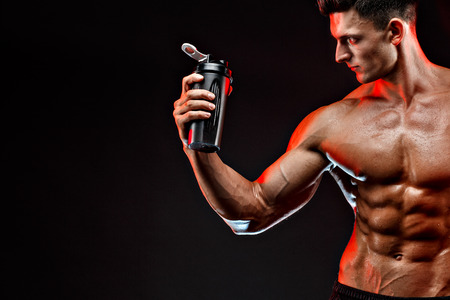 Muscular man with protein drink in shaker over dark backgroundの写真素材