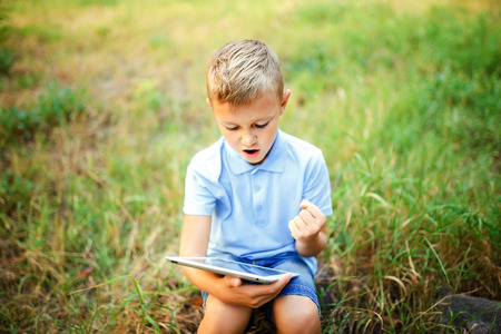 Young kid sittingin the courtyard and playing a game on tablet pc.の写真素材