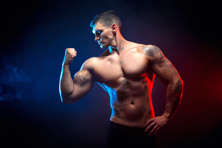 Handsome power athletic man bodybuilder. Fitness muscular body on dark smoke background. Perfect male. Awesome bodybuilder, tattoo, posing.の写真素材
