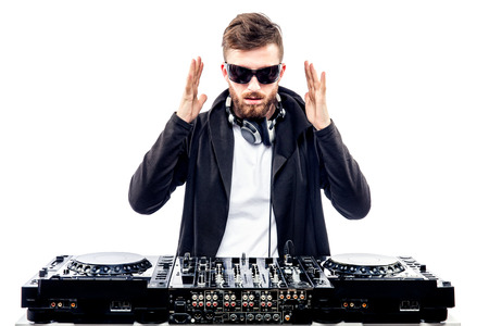 Young stylish man in black sunglasses posing with hands up behind mixing console on white studio background.の写真素材