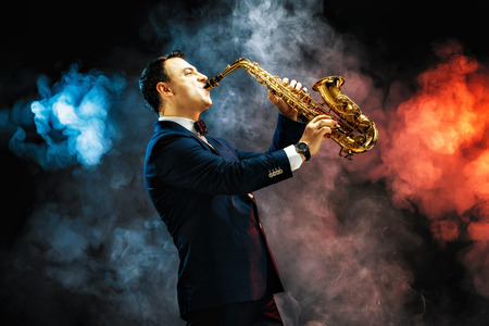 Elegant handsome man playing saxophone in studio against of blue and red smokeの写真素材