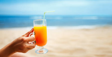 Hand holding Juice in a glass on blurred seascape backgroundの写真素材