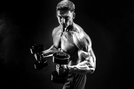 Handsome bodybuilder doing exercise with dumbbell. Studio shot. Black and white photo. Smokeの写真素材