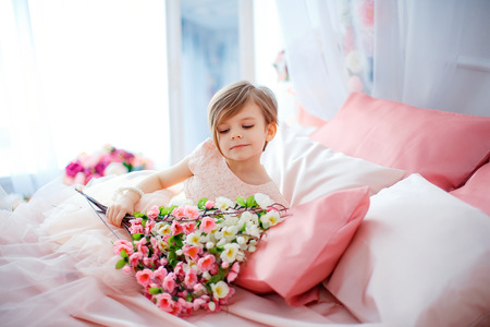 Little nice girl in dress lying on bed with flowers and looking away.の写真素材