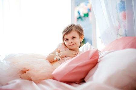 Little nice girl in dress lying on bed with flowers and looking at camera.の写真素材