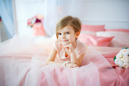 Little nice girl in dress lying on bed with flowers and looking at camera.の写真素材