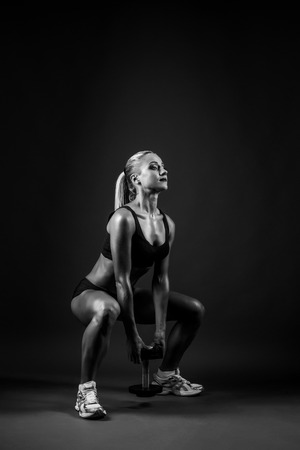 Beautiful muscular woman doing leg exercise on a dark gray background in studio.の写真素材