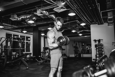 Handsome muscular man is working out and posing with dumbbells at a gymの写真素材