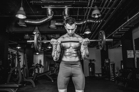Young handsome caucasian bodybuilder sportsman working out with a barbell in gym, doing biceps training.の写真素材