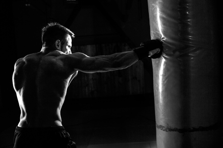 Young male boxer hitting punching bag on black background.の写真素材