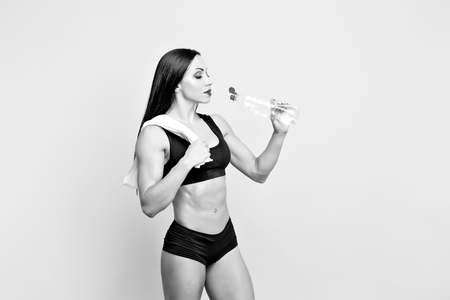 Muscular woman in black leggings, top having a rest, standing and drinking water from the plastic bottleの写真素材