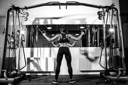 woman flexing muscles on cable machine in gym. exercise on biceps. back viewの写真素材