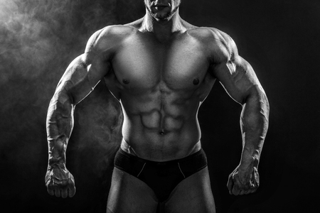 Close up on perfect abs. Strong bodybuilder with six pack.Strong bodybuilder man with perfect abs, shoulders,biceps, triceps and chest, personal fitness trainer flexing his muscles in blue, red smokeの写真素材