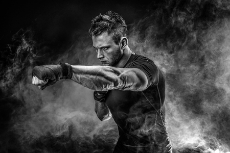 Studio portrait of fighting muscular man in smoke on black backgroundの写真素材