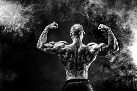 unrecognizable tattoed bodybuilder with outstretched arms on black background. Isolated.の写真素材