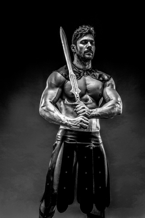 Portrait of handsome muscular gladiator with sword. Studio shot. Black background.の写真素材
