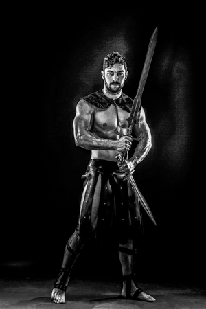 Portrait of handsome muscular gladiator with sword. Studio shot. Black background.の写真素材