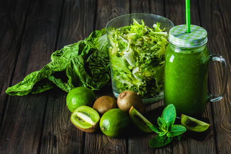 Blended green smoothie with ingredients on wooden table selective focusの写真素材