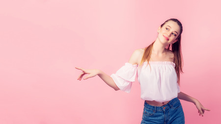 Copy space for advertisement. Colorful portrait of happy smiling young woman pointing away against pink wall.の写真素材