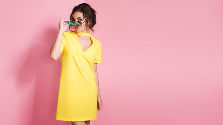 Beautiful girl in colorful clothes wearing sunglasses posing on pink background in studio.の写真素材