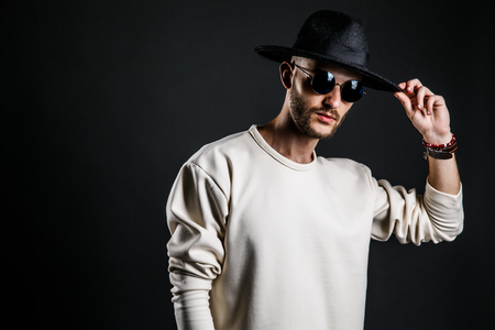 Cool stylish handsome man wearing sunglasses holding hat. Horizontal studio shot.の写真素材