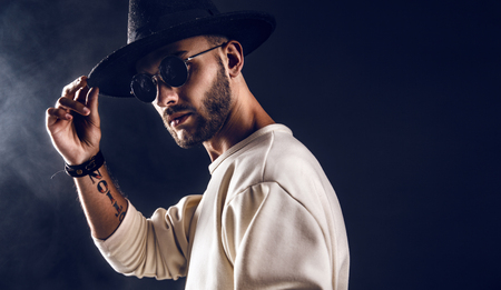 Cool stylish handsome man wearing sunglasses holding hat. Horizontal studio shot.の写真素材