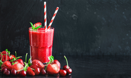 Glass with two straws filled with strawberry smoothie on black with strawberries.の写真素材