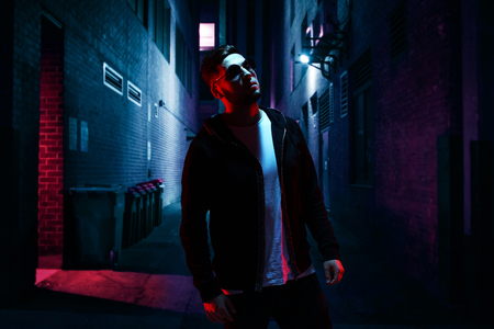 Cool man in sunglasses standing on empty alley at night.