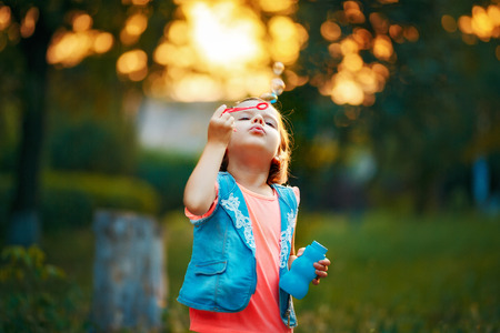 Five years old caucasian child girl blowing soap bubbles outdoor at sunset - happy carefree childhoodの写真素材
