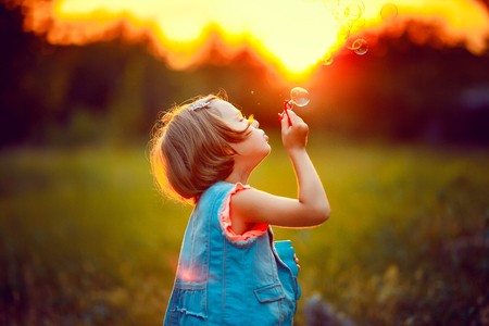 Five years old caucasian child girl blowing soap bubbles outdoor at sunset - happy carefree childhoodの写真素材