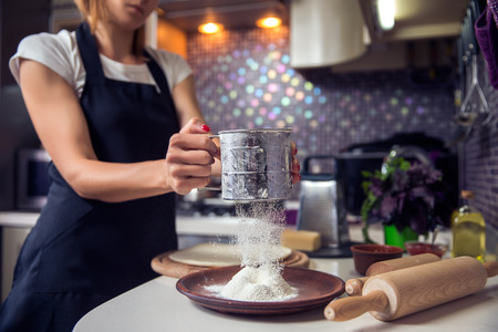 Woman sifting flour through sieve In the kitchen. Selective focus.の写真素材