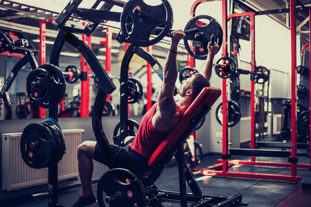 Sports guy doing exercise for the shoulders on the simulator in the gym. Brutal sports man. Bodybuilder on training in the gym. Health and fitnessの写真素材