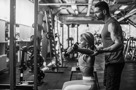 Sporty girl doing weight exercises with assistance of her personal trainer at public gym.の写真素材