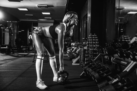 Attractive female athlete performing a kettle-bell swing in crossfit gym.の写真素材
