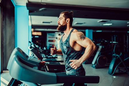 Fit Muscle Bearded Man With Headphones Running on Treadmill in Gym.の写真素材