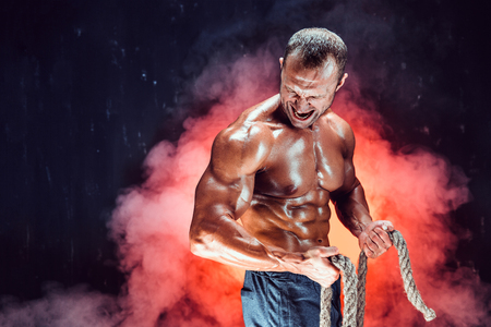 Strong shirtless bodybuilder man working out hard with rope.の写真素材