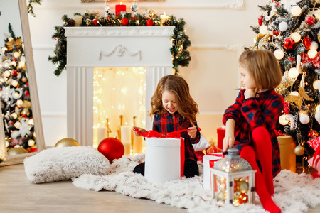 Two adorable girls in checkered dresses sitting near Christmas tree and opening their presents.の写真素材