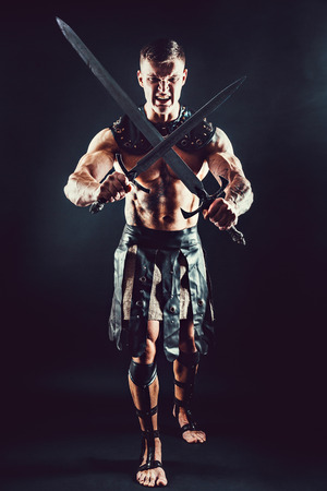 Portrait of handsome muscular gladiator crossed two swords. Studio shot. Black background. Scream.の写真素材
