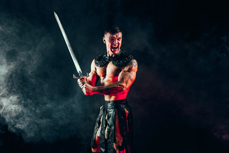 Portrait of handsome muscular gladiator with sword. Studio shot. Smoke on background. Scream.の写真素材