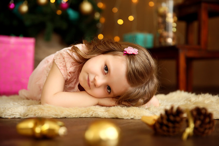 Little charming girl lies near a Christmas tree and looking at camera.の写真素材