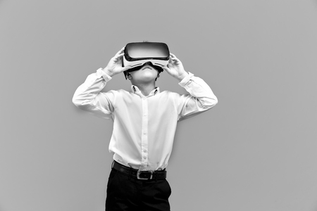 Kid in formal outfit wearing VR glasses putting hands on it in excitement isolated on grey background.の写真素材