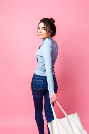 Cheerful casual young woman with bag looking at camera on pink background.の写真素材