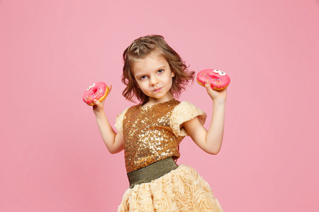 Adorable little girl in dress with donuts with eyes posing on pink background.の写真素材