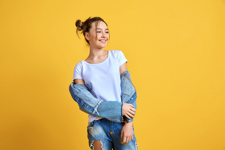 Cheerful young woman in denim clothes standing on yellow background in studio.の写真素材