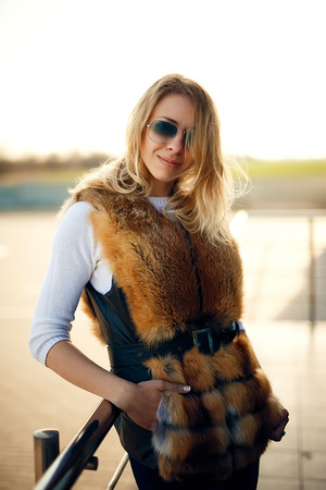 Beautiful blonde woman outdoors in a fur vest and sunglassesの写真素材
