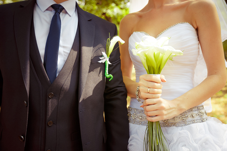 Bride holding beautiful white wedding flowers bouquet. groom standing behind with same flowers in boutonniereの写真素材