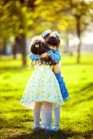 Little pretty girls having fun outdoor. Two cute girls are standing on green grass and hugging. Best friends.の写真素材