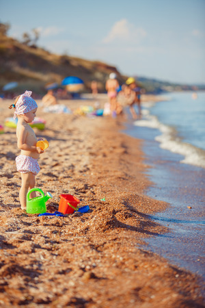 Cute little girl sitting on the beach and playing with plastic toys.の写真素材