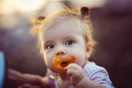 Cute little infant girl standing with dummy and looking at camera outdoors.の写真素材