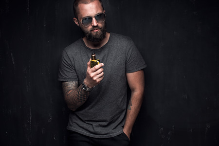 Men with beard in sunglasses vaping and releases a cloud of vapor on dark moody studio background.の写真素材